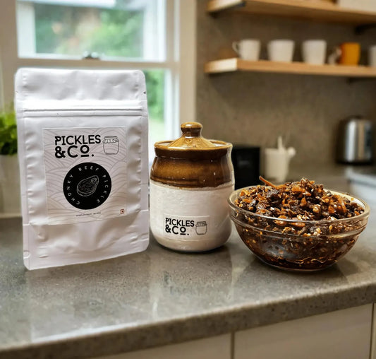 A jar of beef pickle and its packaging on a kitchen counter, with the brand 'PICKLES & CO' visible on the label. A bowl of the pickle is also visible in the foreground.