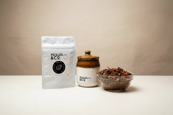 A jar of beef pickle and its packaging on a kitchen counter, with the brand 'PICKLES & CO' visible on the label. A bowl of the pickle is also visible in the foreground.